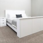 white bed with pillows and blanket and side cabinet