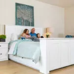 family on a white bed with a tv coming out of the footbed